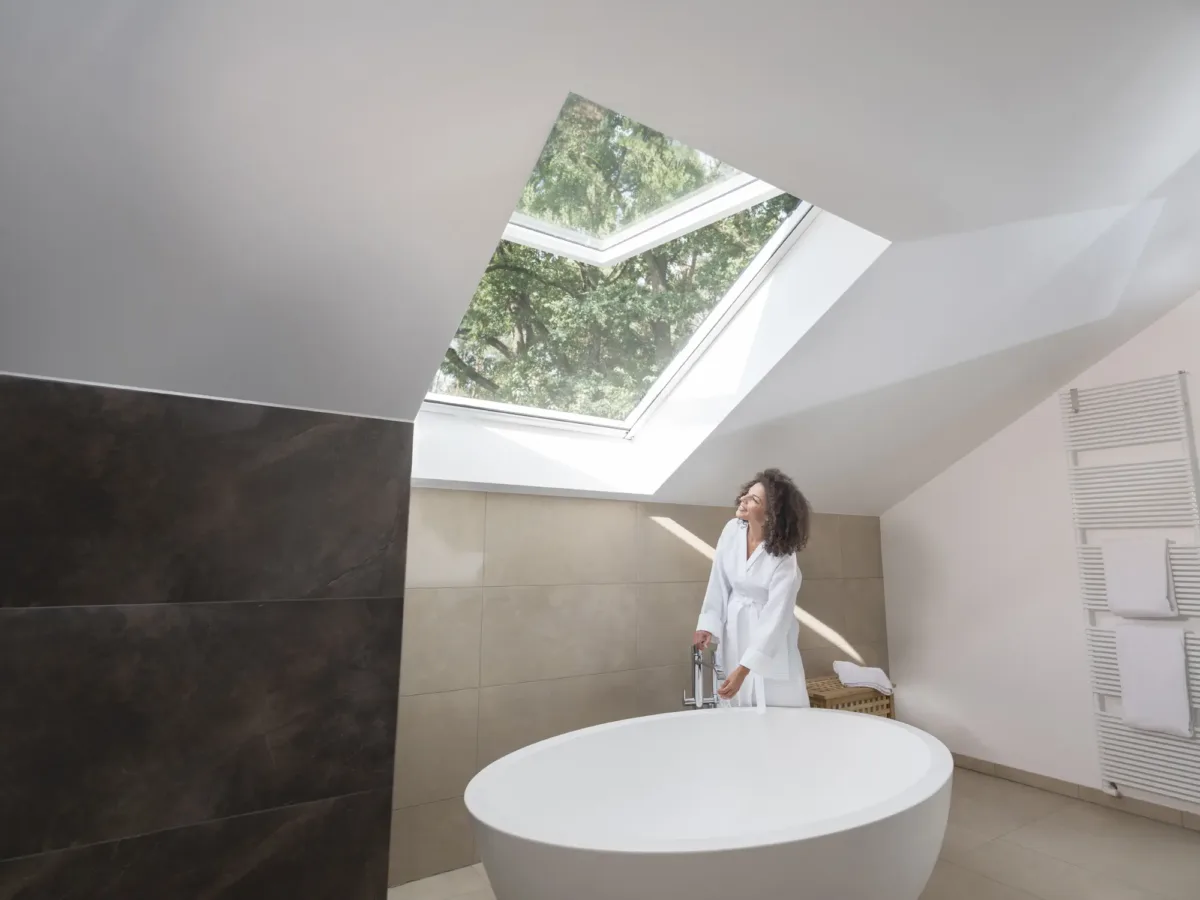 Frau öffnet Dachfenster mit Insektenschutz Rollo in hellem Badezimmer