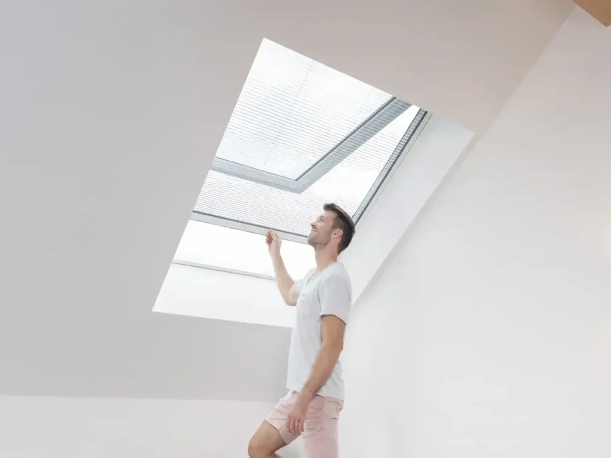 Mann bedient Plissee Fliegengitter am Dachfenster in hellem Zimmer